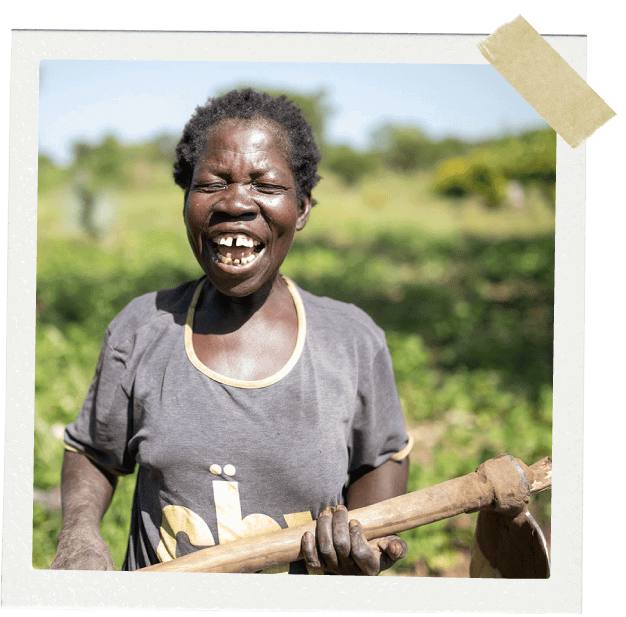 African woman with farming equipment smiling.